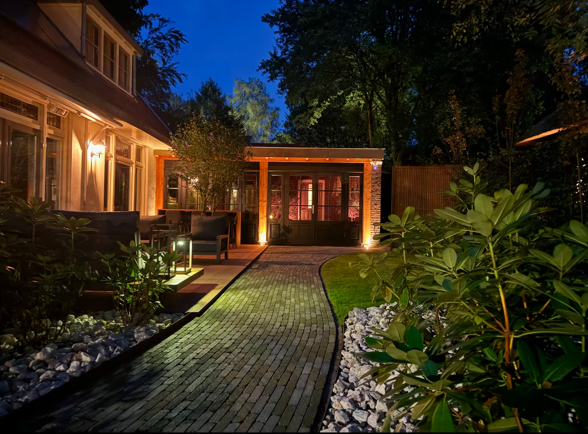 Het bijgebouw in de avond, gezien vanaf het verlichte tuinpad